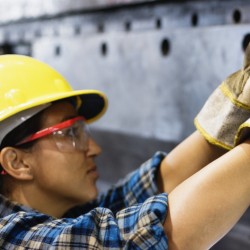 Female manual worker drilling holes in sheet metal in factory